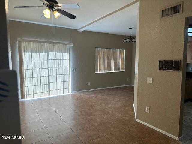 unfurnished room featuring baseboards, visible vents, and ceiling fan with notable chandelier