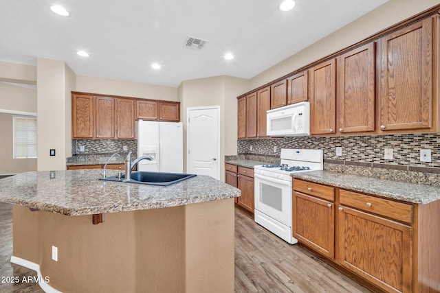 11318 W Monte Vista Rd, Avondale, AZ 85392 - kitchen with white appliances, light wood-style floors, a kitchen island with sink, decorative backsplash, and brown cabinets