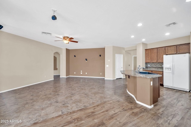 11318 W Monte Vista Rd, Avondale, AZ 85392 - kitchen featuring white refrigerator with ice dispenser, ceiling fan, arched walkways, a kitchen island with sink, and light stone countertops
