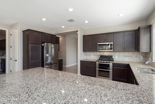 20644 W Mariposa St, Buckeye, AZ 85396 - kitchen featuring stainless steel appliances, a sink, dark brown cabinetry, light stone counters, and tasteful backsplash