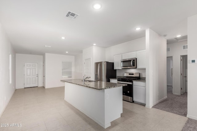 kitchen featuring sink, dark stone countertops, appliances with stainless steel finishes, an island with sink, and white cabinets