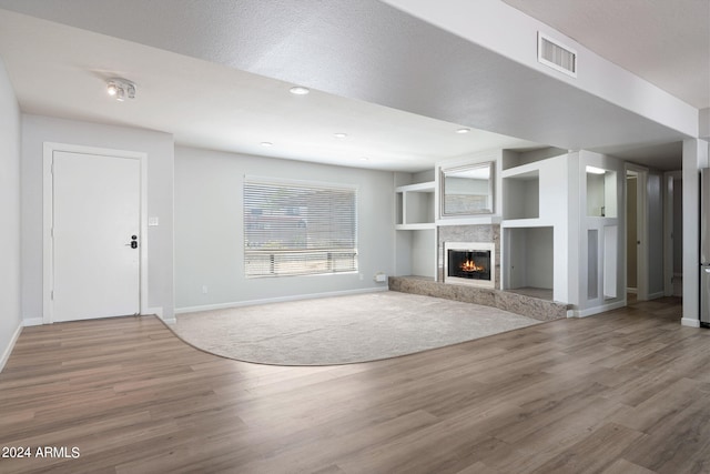 unfurnished living room featuring a fireplace, built in shelves, hardwood / wood-style floors, and a textured ceiling