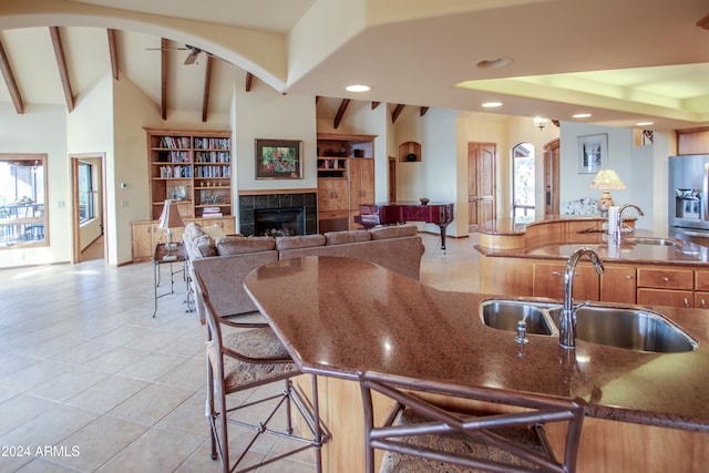 kitchen with sink, vaulted ceiling with beams, built in features, light tile patterned floors, and a tiled fireplace