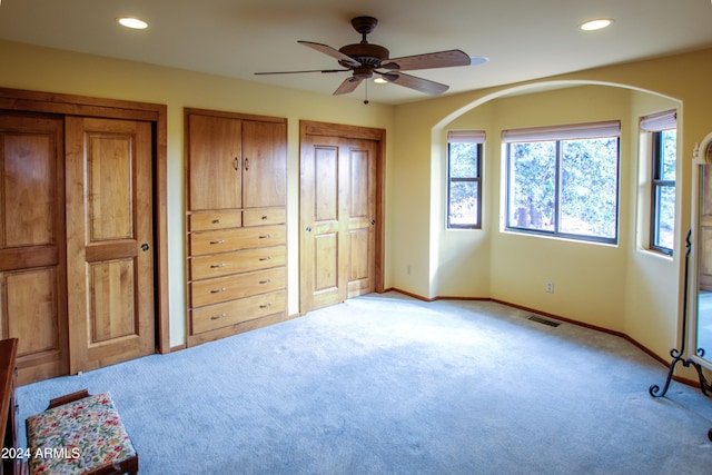 unfurnished bedroom featuring ceiling fan, light carpet, and two closets