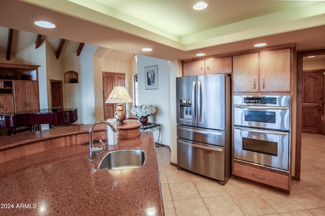 kitchen featuring stone counters, sink, stainless steel appliances, vaulted ceiling with beams, and light tile patterned floors