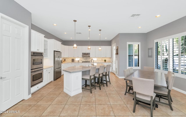 kitchen with a center island with sink, pendant lighting, light stone countertops, stainless steel appliances, and white cabinets