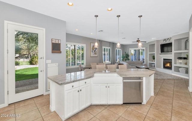 kitchen with dishwasher, white cabinetry, a kitchen island with sink, built in features, and light stone counters