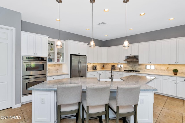 kitchen featuring appliances with stainless steel finishes, a center island with sink, tasteful backsplash, and decorative light fixtures