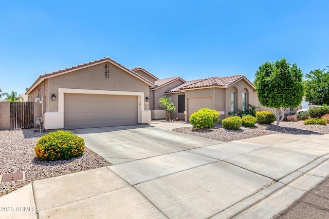 view of front of house with a tile roof, a garage, stucco siding, a gate, and concrete driveway