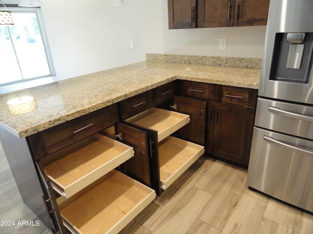 kitchen featuring dark brown cabinetry, light stone countertops, stainless steel refrigerator with ice dispenser, kitchen peninsula, and light wood-type flooring