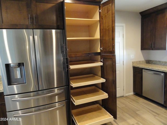 kitchen featuring light stone countertops, dark brown cabinets, light wood-type flooring, and appliances with stainless steel finishes