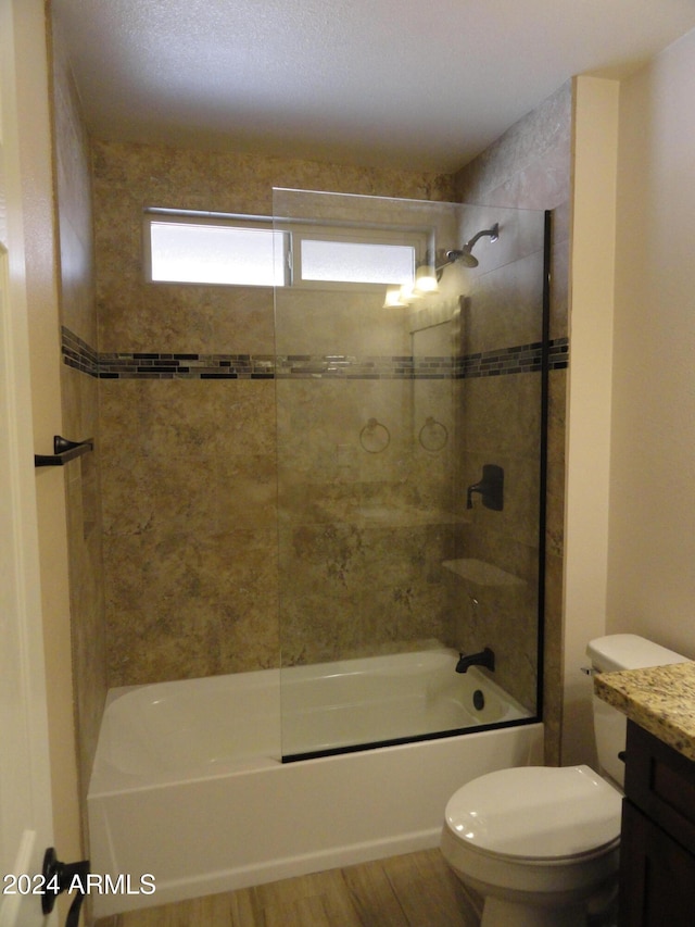 full bathroom with hardwood / wood-style floors, vanity, tiled shower / bath, toilet, and a textured ceiling