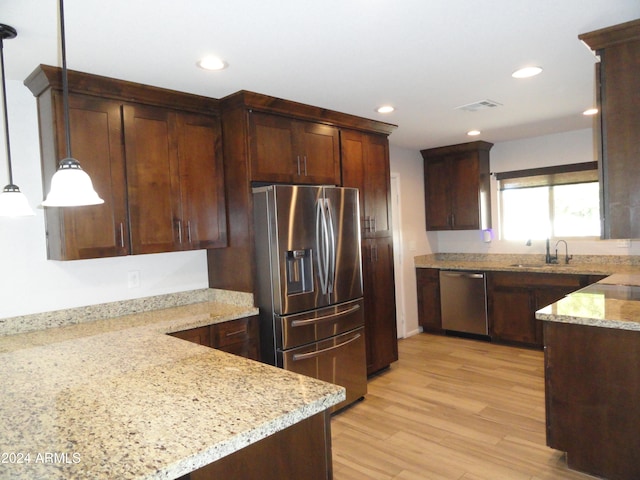 kitchen with dark brown cabinetry, light stone countertops, stainless steel appliances, pendant lighting, and light hardwood / wood-style floors