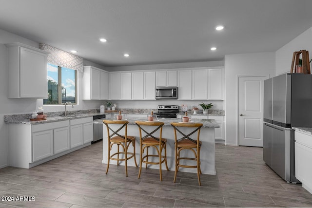 kitchen featuring stainless steel appliances, white cabinets, light stone counters, and a kitchen island