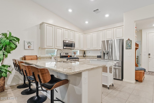 kitchen with kitchen peninsula, a kitchen bar, stainless steel appliances, and light stone countertops