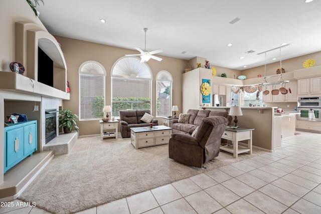 living room featuring light tile patterned floors, visible vents, light colored carpet, and a glass covered fireplace