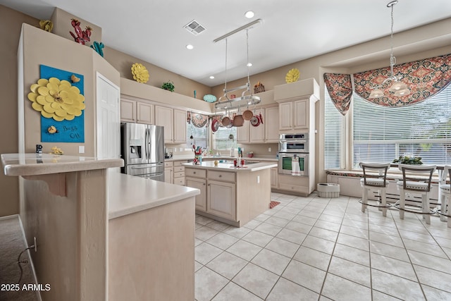 kitchen with visible vents, a kitchen island, stainless steel appliances, light countertops, and cream cabinetry