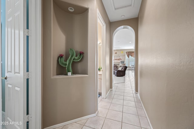 corridor featuring light tile patterned floors, arched walkways, and baseboards