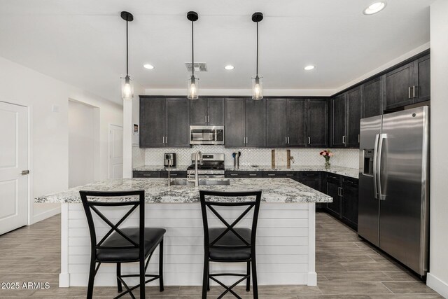 1567 W Camina Plata, San Tan Valley, AZ 85140 - kitchen featuring appliances with stainless steel finishes, light stone counters, decorative backsplash, a breakfast bar area, and recessed lighting