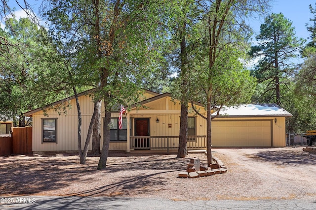 view of front of property with a porch, fence, a garage, and dirt driveway