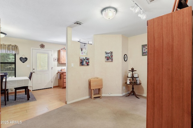 hall with light wood-type flooring, visible vents, light carpet, rail lighting, and baseboards