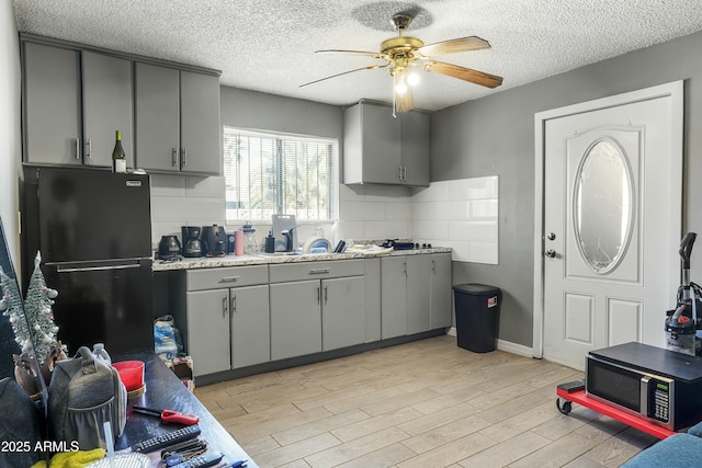 kitchen featuring gray cabinetry, ceiling fan, black refrigerator, and sink