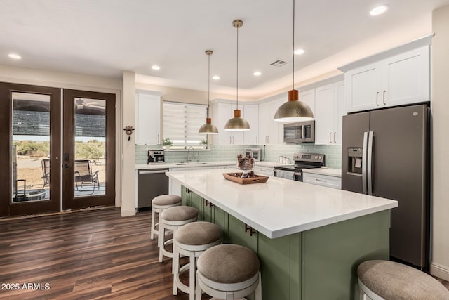 kitchen featuring stainless steel appliances, light countertops, white cabinets, a sink, and a kitchen bar