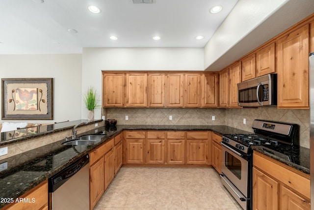 kitchen featuring stainless steel appliances, recessed lighting, backsplash, a sink, and dark stone countertops