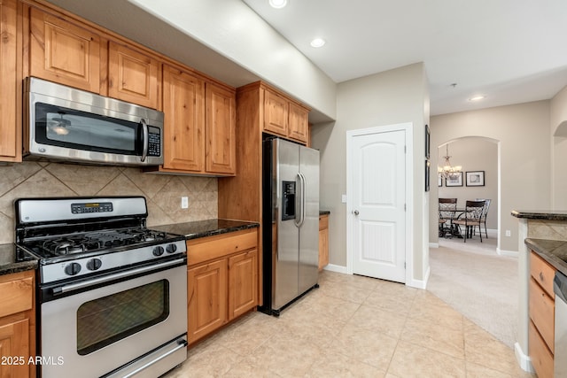 kitchen with arched walkways, a chandelier, stainless steel appliances, baseboards, and decorative backsplash