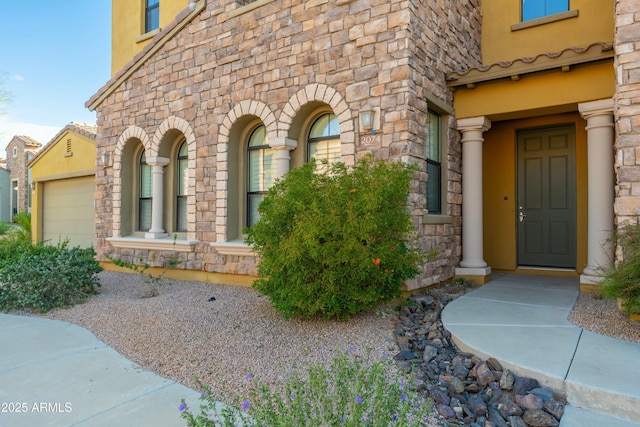 property entrance with stone siding, an attached garage, and stucco siding