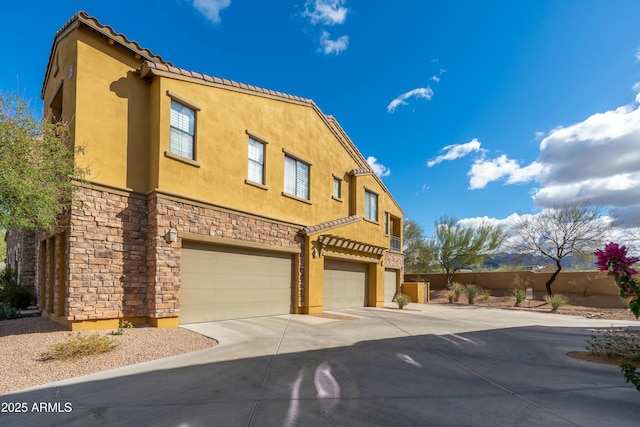 view of front facade featuring a garage, concrete driveway, stone siding, fence, and stucco siding