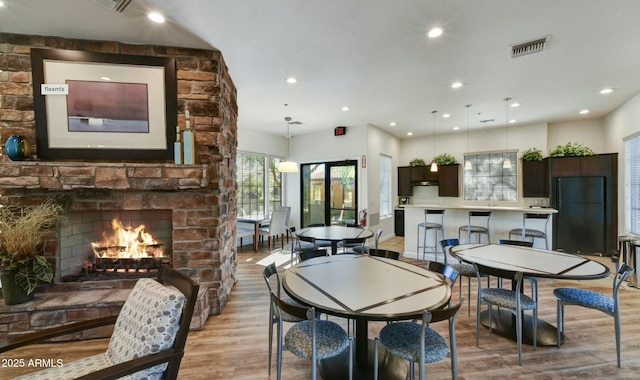 dining room featuring light wood-type flooring, a large fireplace, visible vents, and recessed lighting