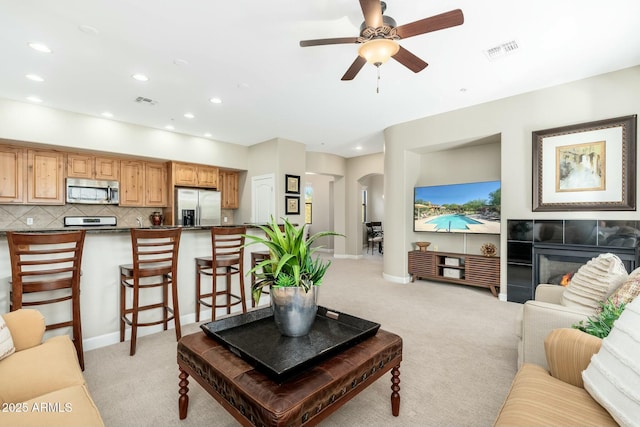 living area with visible vents, arched walkways, a glass covered fireplace, and light colored carpet