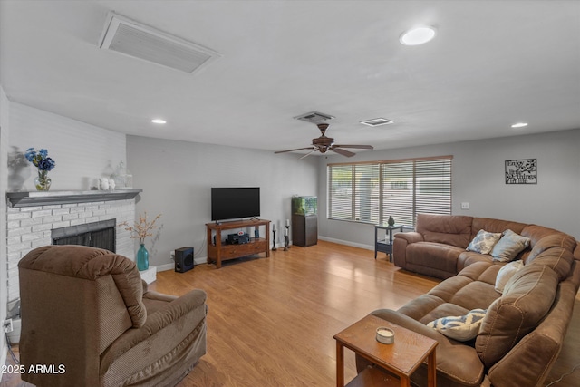 living area with light wood finished floors, a brick fireplace, visible vents, and ceiling fan