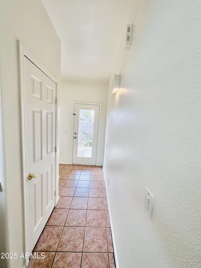 doorway to outside featuring light tile patterned floors and a textured ceiling