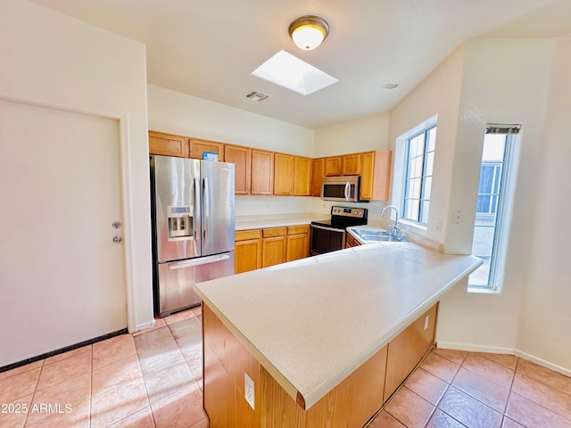 kitchen featuring kitchen peninsula, appliances with stainless steel finishes, a skylight, and sink