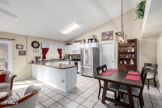 kitchen featuring vaulted ceiling, kitchen peninsula, pendant lighting, stainless steel appliances, and white cabinets