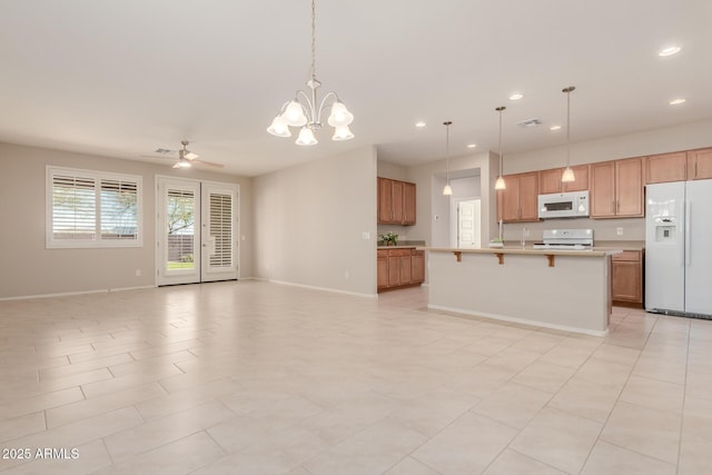 kitchen featuring white appliances, decorative light fixtures, a kitchen bar, a kitchen island with sink, and ceiling fan with notable chandelier