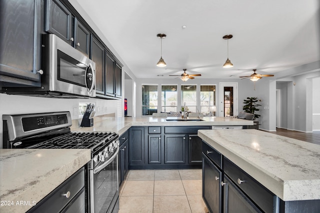 kitchen featuring appliances with stainless steel finishes, light tile patterned flooring, kitchen peninsula, decorative light fixtures, and sink