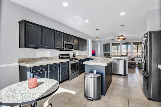 kitchen featuring kitchen peninsula, a kitchen island, appliances with stainless steel finishes, light tile patterned floors, and decorative light fixtures