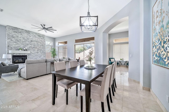 dining space featuring arched walkways, ceiling fan with notable chandelier, a fireplace, visible vents, and baseboards