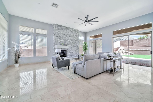 living area featuring ceiling fan, visible vents, a wealth of natural light, and a stone fireplace