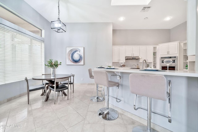 kitchen with light countertops, under cabinet range hood, double oven, a kitchen bar, and open shelves