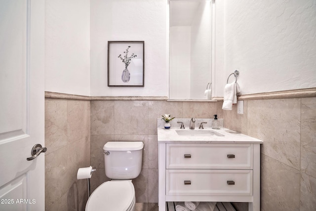 half bathroom with toilet, a wainscoted wall, tile walls, and vanity