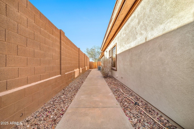 view of side of home with central AC unit, a fenced backyard, and stucco siding