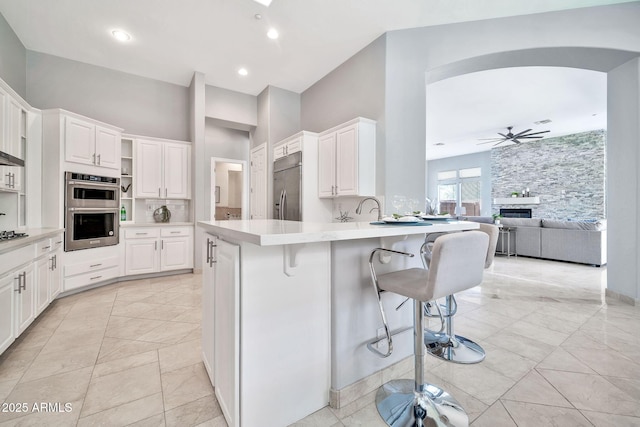 kitchen featuring decorative backsplash, a breakfast bar, stainless steel appliances, light countertops, and white cabinetry