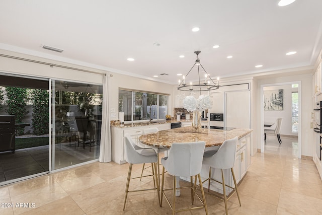 kitchen featuring pendant lighting, a kitchen island with sink, a notable chandelier, white cabinetry, and light stone countertops