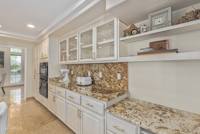 kitchen featuring light stone counters, white cabinets, double oven, and tasteful backsplash