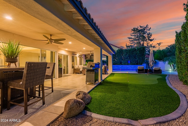 yard at dusk with ceiling fan, a pool, outdoor lounge area, and a patio area