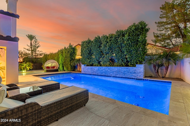 pool at dusk featuring a patio and pool water feature